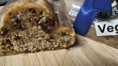 Veganer Dinkelstollen mit sichtbarem inneren Teig und Trockenfrüchten, auf einem Holzbrett präsentiert.